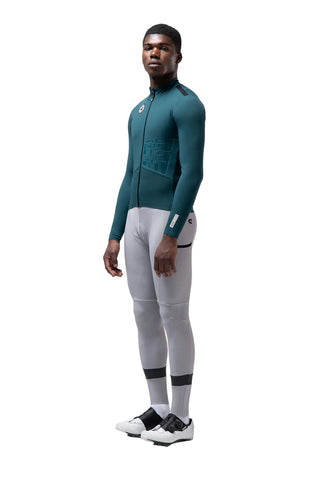 Ciclista uomo con giacca Gobik Element Sunken verde petrolio e pantaloni grigi, abbigliamento tecnico per bici da corsa.