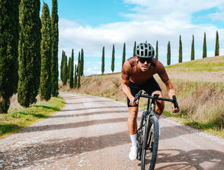 Ciclista su gravel bike pedala su una strada sterrata tra cipressi toscani, godendosi un’avventura all’aria aperta.
