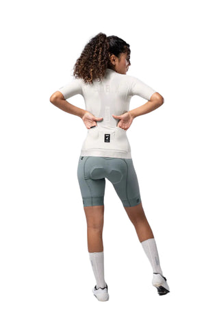 Vista posteriore della maglia Gobik CX Solid Argonite avorio indossata da una ciclista, con mani nelle tasche.